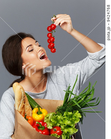 Smiling brunette woman with grocery bag full of fresh vegetables and cherry tomatoes Smiling brunette woman with grocery bag full of fresh vegetables and cherry tomatoes 9424768