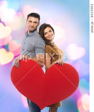 Happy couple in shirt and dress holding handmade paper heart over blurred background 9425003