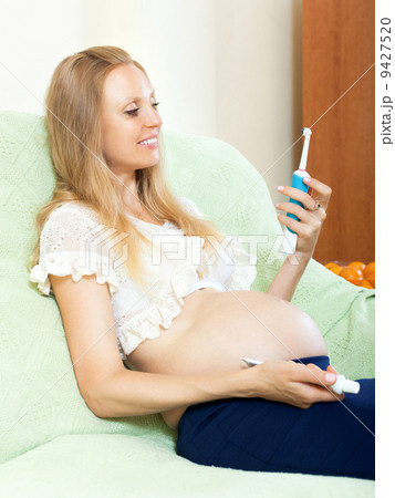 Smiling cute pregnant blond with dental cleaning brush at home Smiling cute pregnant blond with dental cleaning brush at home 9427520