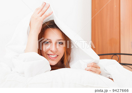 girl in a shirt lying on the snow-white sheets on the bed at hom 9427666