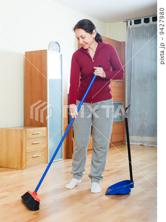 mature housewife with dustpan and brush at home 9427980
