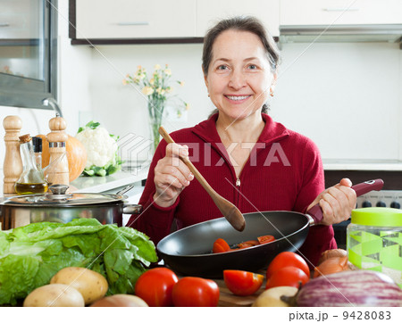 Positive mature woman cooking with skillet 9428083