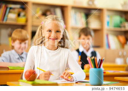 Little schoolgirl sitting behind school desk during lesson in school 9474653