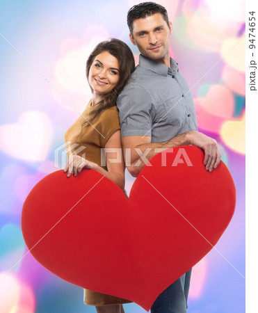 Happy couple in shirt and dress holding handmade paper heart over blurred background 9474654