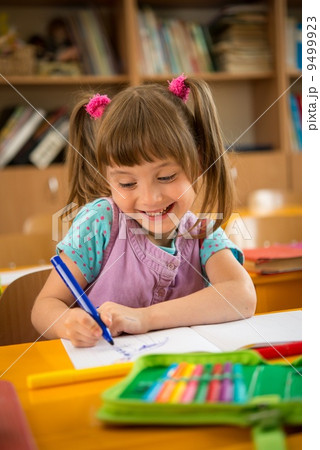 Little schoolgirl sitting behind school desk during lesson in school 9499923