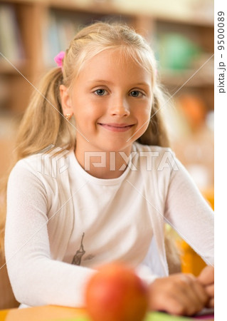Little schoolgirl sitting behind school desk during lesson in school 9500089