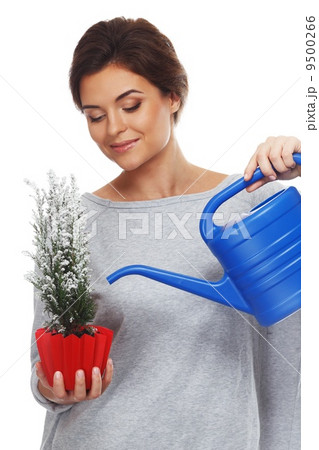 Beautiful brunette woman watering plant in red pot Beautiful brunette woman watering plant in red pot 9500266