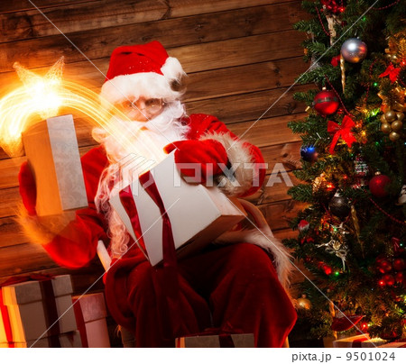 Santa Claus in wooden home interior holding gift box with magic star flying out of it Santa Claus in wooden home interior holding gift box with magic star flying out of it 9501024