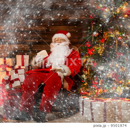 Santa Claus sitting on rocking chair in wooden home interior with letters in hands 9501974
