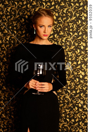 Beautiful young girl with glass of wine wearing black evening dress in luxury interior Beautiful young girl with glass of wine wearing black evening dress in luxury interior 9502039