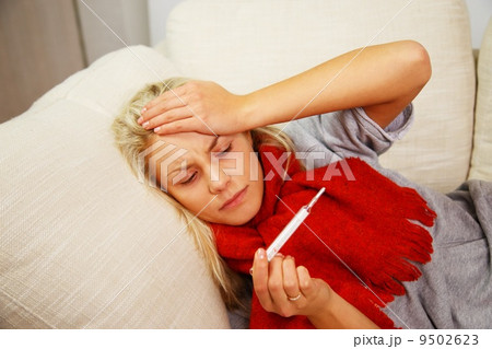 Sick young woman with thermometer lying on sofa at home 9502623