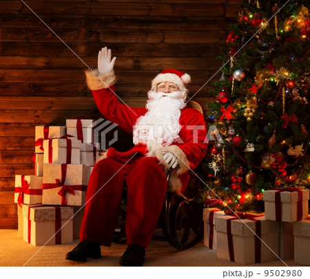 Santa Claus sitting on rocking chair in wooden home interior with gift boxes around him 9502980