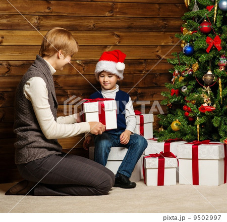 Mother and her lIttle boy in Santa hat with gift box under christmas tree in wooden house interior Mother and her lIttle boy in Santa hat with gift box under christmas tree in wooden house interior 9502997