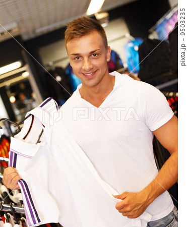 Handsome young man choosing t-shirt in a sport outlet 9503235