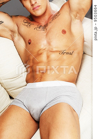 Man with beautiful muscular tattooed torso in underwear lying on sofa 9503664