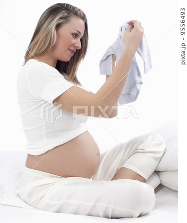 Beautiful Pregnant Young Woman Holding Up New Baby Clothes, Waiting For Her Baby To Be Born Beautiful Pregnant Young Woman Holding Up New Baby Clothes, Waiting For Her Baby To Be Born 9556493