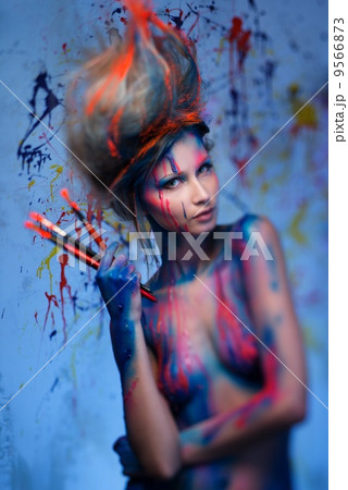 Young woman muse with creative body art and hairdo holding paint brushes 9566873