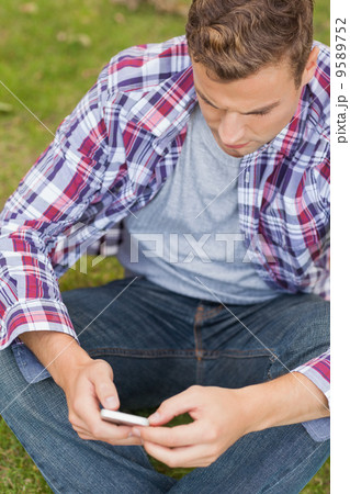Handsome unsmiling student sitting on grass texting 9589752