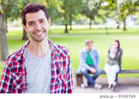 College boy smiling with blurred students sitting in park 9589769