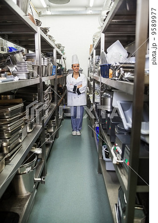 Young pretty chef standing arms crossed between shelves 9589977