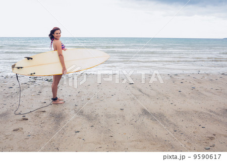 Smiling woman carrying surfboard on the beach 9590617