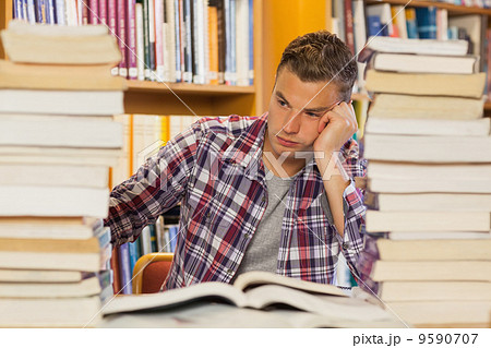 Frustrated handsome student studying between piles of books 9590707