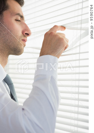 Attractive stern businessman spying through roller blind Attractive stern businessman spying through roller blind 9590764