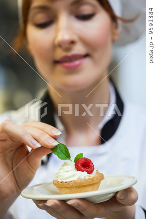 Focused head chef putting mint leaf on little cake on plate 9591384