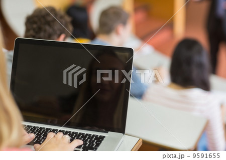 Female using laptop with students and teacher at lecture hall Female using laptop with students and teacher at lecture hall 9591655
