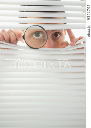 Male eyes spying through roller blind with magnifier 9591795