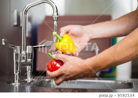 Kitchen porter washing pepper under running tap Kitchen porter washing pepper under running tap 9592534