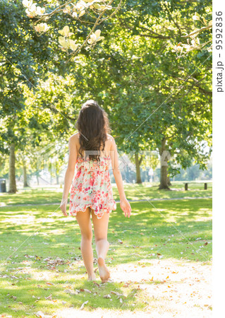 Rear view of stylish brunette walking on grass 9592836