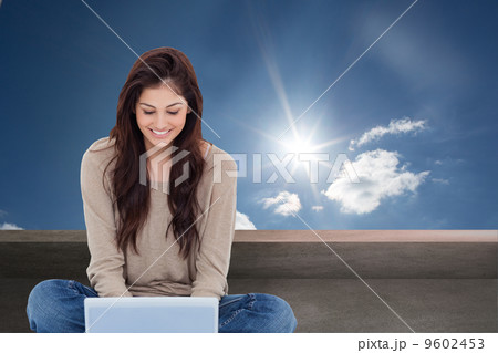 Composite image of brunette sitting on floor using laptop 9602453