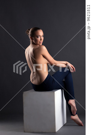 Slim topless girl sitting on cube, back to camera 9621811