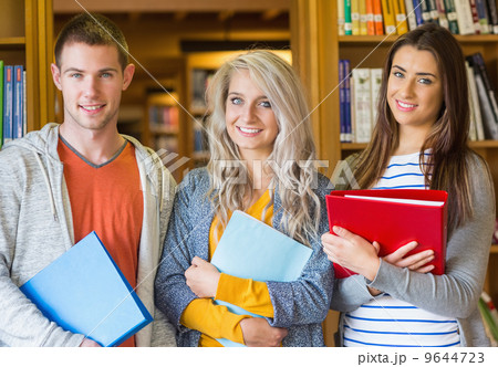 Students with folders standing against bookshelf in library Students with folders standing against bookshelf in library 9644723