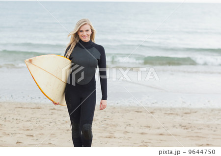 Smiling woman in wet suit holding surfboard at beach 9644750