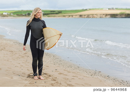 Beautiful woman in wet suit holding surfboard at beach 9644968