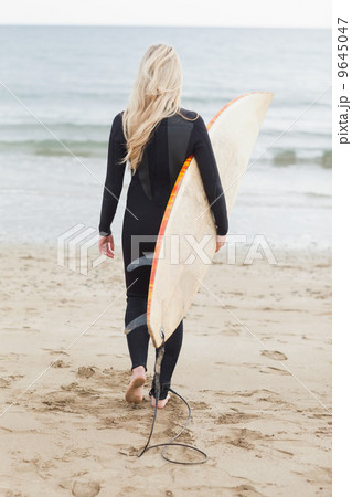 Rear view of a woman in wet suit holding surfboard at beach Rear view of a woman in wet suit holding surfboard at beach 9645047