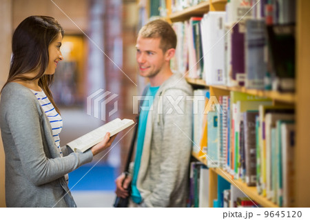 Couple standing against bookshelf in library Couple standing against bookshelf in library 9645120