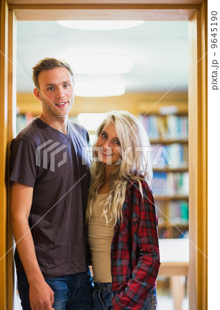 Smiling couple against blurred bookshelf in library 9645190