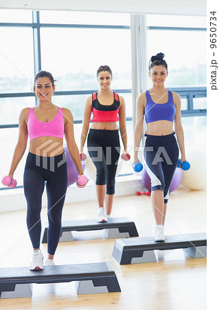 Fitness class performing step aerobics exercise with dumbbells 9650734