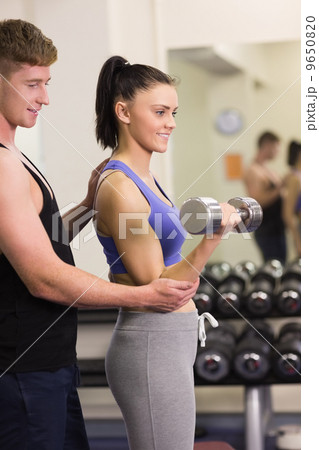 Male trainer helping young woman with the dumbbells in gym Male trainer helping young woman with the dumbbells in gym 9650820
