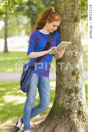 Happy student leaning against a tree using her tablet pc 9651118