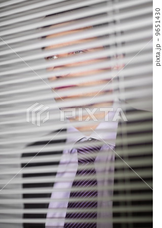 Businessman peeking through blinds in office Businessman peeking through blinds in office 9651430