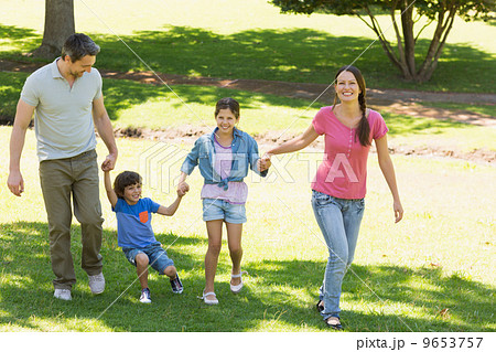Family of four holding hands and walking at park 9653757