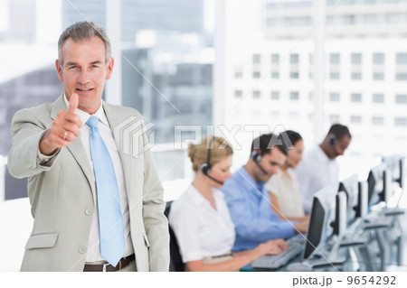 Businessman gesturing thumbs up with executives using computers Businessman gesturing thumbs up with executives using computers 9654292