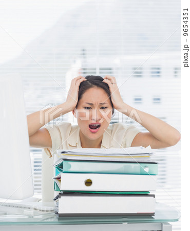 Angry businesswoman shouting with stack of folders at desk 9654351