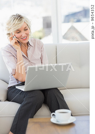 Businesswoman using mobile phone and laptop at home 9654352