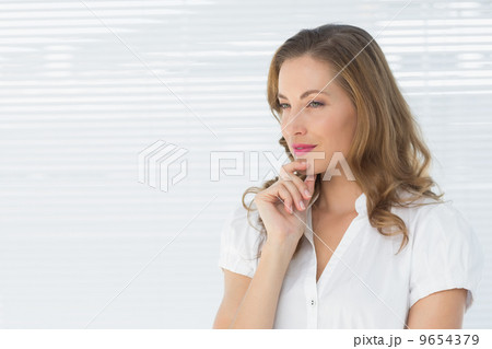 Thoughtful businesswoman looking away against blinds 9654379