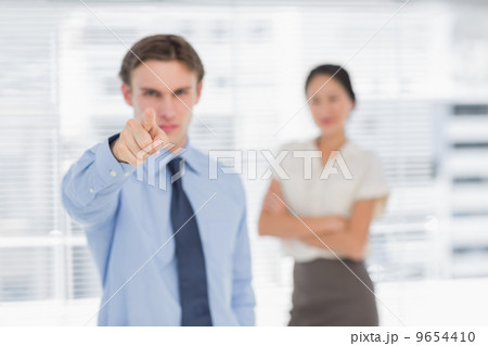 Businessman pointing towards camera with woman in office Businessman pointing towards camera with woman in office 9654410